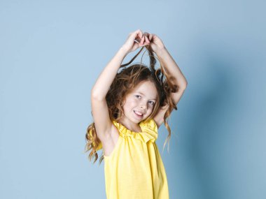 mavi arka planda poz verirken sarı üst gülümseyen güzel esmer kız saç ile oynarken