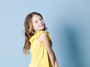 mavi arka plan önünde poz sarı üst gülümseyen ürkek esmer kız yan görünümü