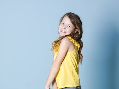 mavi arka plan önünde poz sarı üst gülümseyen ürkek esmer kız yan görünümü