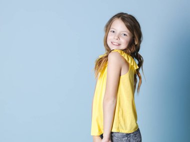 mavi arka plan önünde poz sarı üst gülümseyen ürkek esmer kız yan görünümü