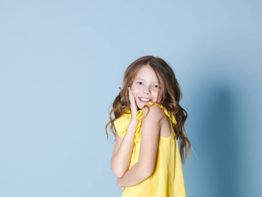 sarı üst gülümseyen güzel esmer kız yanak dokunmadan ve mavi arka plan önünde kameraya bakarak 