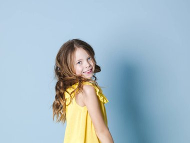 mavi arka plan önünde poz sarı üst gülümseyen ürkek esmer kız yan görünümü