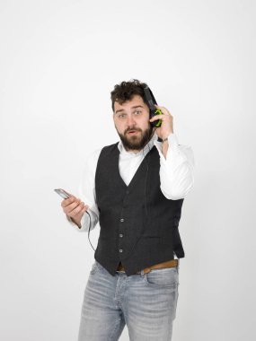 siyah sakallı komik adam kulaklık müzik dinlerken ve beyaz stüdyo duvar önünde poz verirken akıllı telefon tutarak