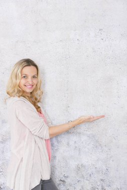 gri arka plan önünde poz verirken boş alan gösteren güzel sarışın kadın