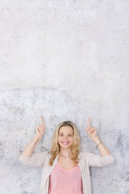 güzel sarışın kadın kaldırdı elleri ile poz ve gri arka plan önünde parmakları işaret
