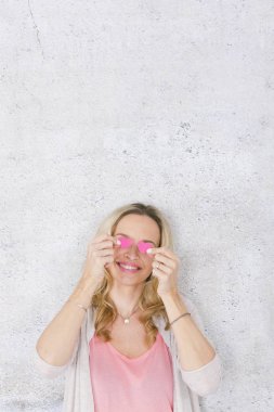 komik romantik sarışın kadın gülümseyen ve gri beton arka plan önünde iki pembe kağıt kalpleri ile poz