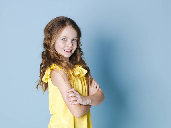 smiling pretty brunette girl in yellow top posing with crossed arms in front of blue background