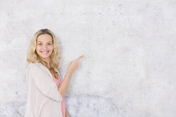 gri arka plan önünde poz verirken kenara işaret güzel sarışın kadın