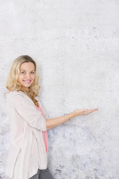 gri arka plan önünde poz verirken boş alan gösteren güzel sarışın kadın