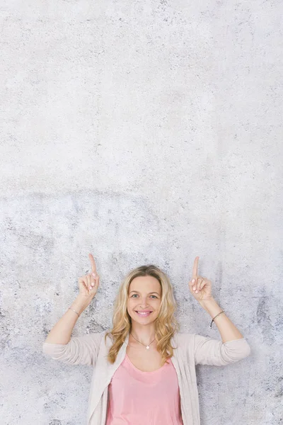 güzel sarışın kadın kaldırdı elleri ile poz ve gri arka plan önünde parmakları işaret