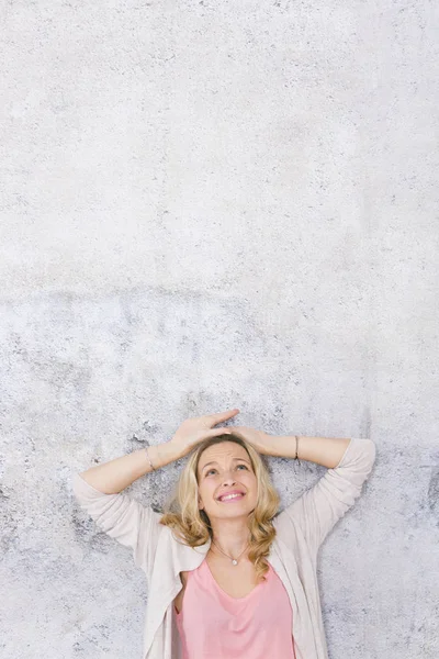 güzel sarışın kadın başının üzerinde elleri ile poz ve gri arka plan önünde bakarak