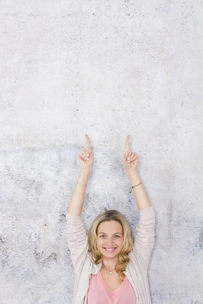 güzel sarışın kadın kaldırdı elleri ile poz ve gri arka plan önünde parmakları işaret