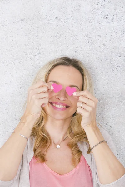komik romantik sarışın kadın gülümseyen ve gri beton arka plan önünde iki pembe kağıt kalpleri ile poz