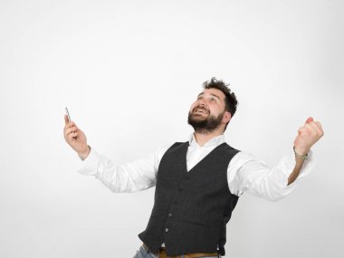 Siyah sakallı genç adam akıllı telefon tutuyor ve kollarını kaldırmış beyaz arka planda zafer kutlamaları yapıyor.