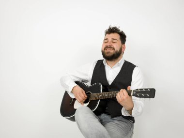 beyaz arka planda akustik gitar çalarken siyah saçlı ve sakallı adam şarkı söylüyor