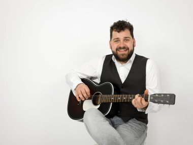 siyah saçlı ve sakallı adam beyaz arka planda akustik gitar çalıyor