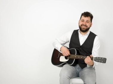 siyah saçlı ve sakallı adam beyaz arka planda akustik gitar çalıyor