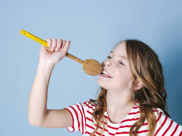 マイクとして調理スプーンを使用し 青い背景の前で歌うかなりクールな小さな女の子 — ストック写真