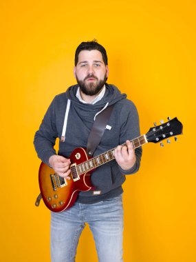 siyah saçlı ve sakallı adam sarı arka plan önünde elektrik gitar çalıyor