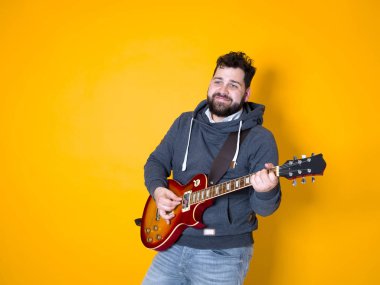 siyah saçlı ve sakallı adam sarı arka plan önünde elektrik gitar çalıyor
