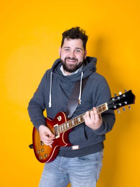 siyah saçlı ve sakallı adam sarı arka plan önünde elektrik gitar çalıyor