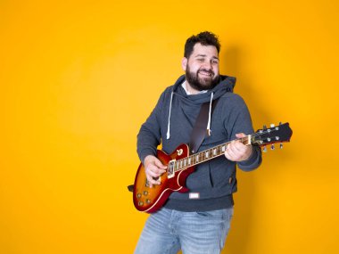 siyah saçlı ve sakallı adam sarı arka plan önünde elektrik gitar çalıyor