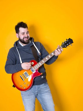 siyah saçlı ve sakallı adam sarı arka plan önünde elektrik gitar çalıyor