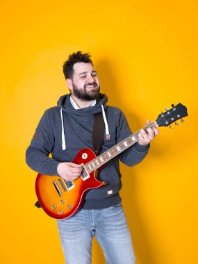 siyah saçlı ve sakallı adam sarı arka plan önünde elektrik gitar çalıyor