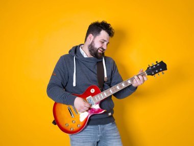 siyah saçlı ve sakallı adam sarı arka plan önünde elektrik gitar çalıyor