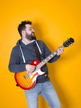 siyah saçlı ve sakallı adam sarı arka plan önünde elektrik gitar çalıyor