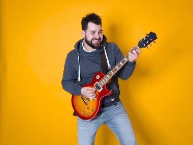 siyah saçlı ve sakallı adam sarı arka plan önünde elektrik gitar çalıyor