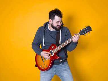 siyah saçlı ve sakallı adam sarı arka plan önünde elektrik gitar çalıyor