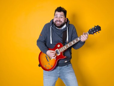 siyah saçlı ve sakallı adam sarı arka plan önünde elektrik gitar çalıyor