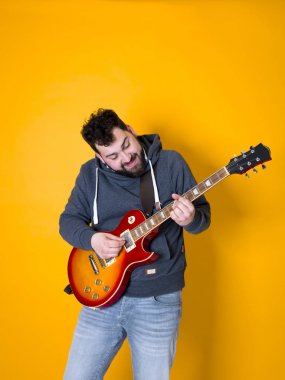 siyah saçlı ve sakallı adam sarı arka plan önünde elektrik gitar çalıyor
