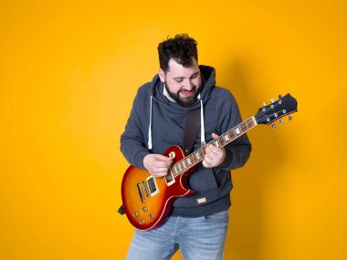 siyah saçlı ve sakallı adam sarı arka plan önünde elektrik gitar çalıyor