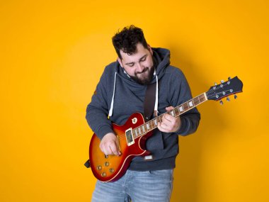 siyah saçlı ve sakallı adam sarı arka plan önünde elektrik gitar çalıyor