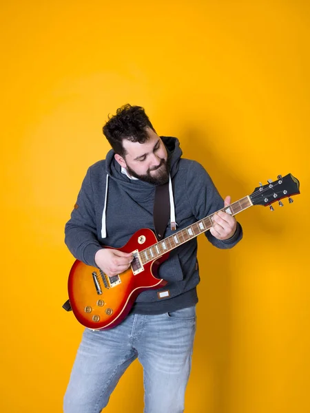 man with black hair and beard playing electric guitar in front of yellow background