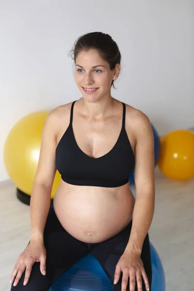ライトスタジオでのフィットネスエクササイズの後に有酸素ボールに座っている間にリラックスした黒のスポーツウェアで美しい若い妊娠中の女性 — ストック写真
