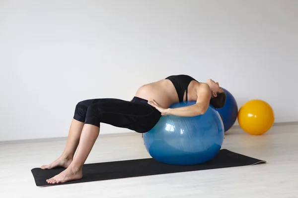 美丽的年轻孕妇在黑色运动服平衡 而躺在有氧球在轻工作室 — 图库照片