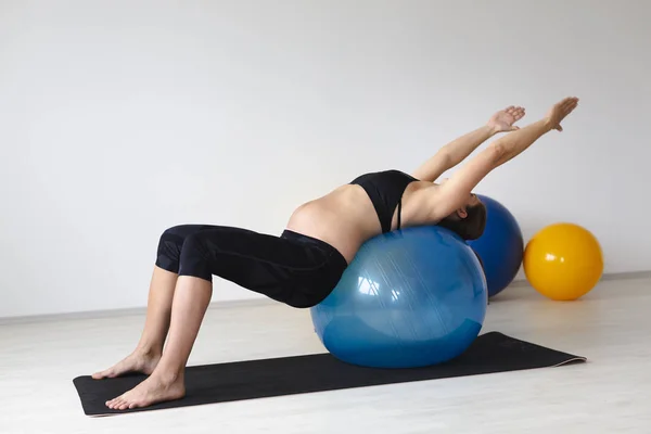 美丽的年轻孕妇在黑色运动服平衡 而躺在有氧球在轻工作室 — 图库照片
