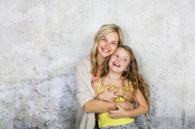 sarışın genç anne beton duvar arka plan üzerinde mutlu gülümseyen kızı kucaklayan  
