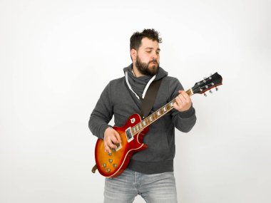 cool man with black hair and beard wearing grey hoodie playing electric guitar in front of white background