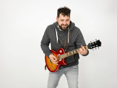 cool man with black hair and beard wearing grey hoodie playing electric guitar in front of white background