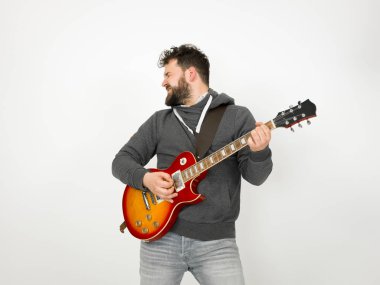 cool man with black hair and beard wearing grey hoodie playing electric guitar in front of white background