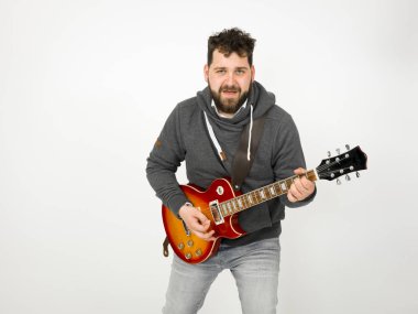 cool man with black hair and beard wearing grey hoodie playing electric guitar in front of white background