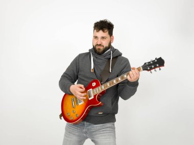 cool man with black hair and beard wearing grey hoodie playing electric guitar in front of white background