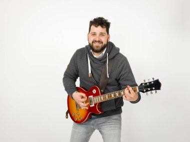 cool man with black hair and beard wearing grey hoodie playing electric guitar in front of white background