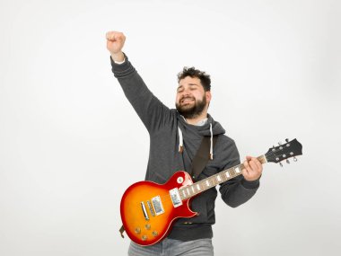 cool man with black hair and beard wearing grey hoodie playing electric guitar in front of white background