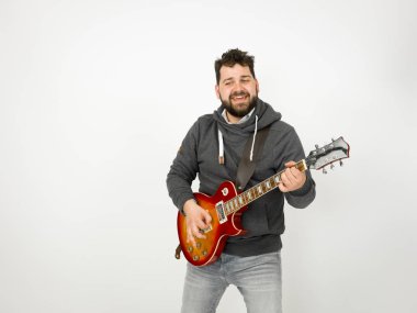 cool man with black hair and beard wearing grey hoodie playing electric guitar in front of white background