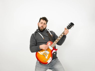 cool man with black hair and beard wearing grey hoodie playing electric guitar in front of white background
